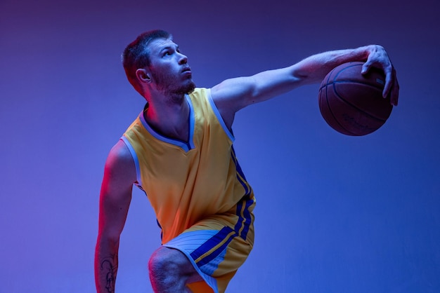 Porträt eines jungen Mannes, der Basketballspieler trainiert, isoliert auf blauem Hintergrund in Neonlicht