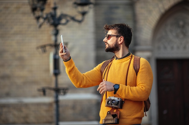 Porträt eines jungen Mannes, der beim Sightseeing in einer fremden Stadt ein Handy hält