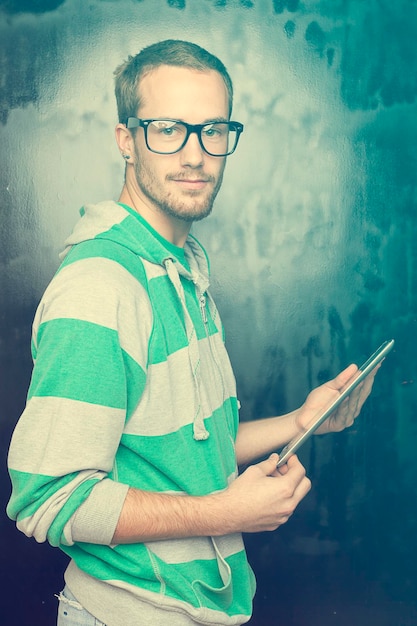 Foto porträt eines jungen mannes, der ein digitales tablet benutzt, während er gegen eine alte wand steht