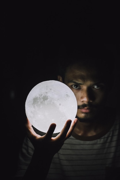 Foto porträt eines jungen mannes, der eine beleuchtete kugel vor schwarzem hintergrund hält