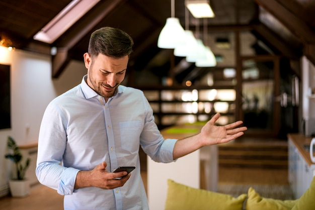 Porträt eines jungen Mannes, der Handy mit verwirrtem Ausdruck auf Gesicht betrachtet