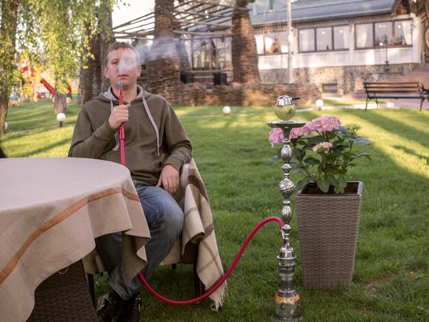 Foto porträt eines jungen mannes, der in einem garten eine wasserpfeife raucht