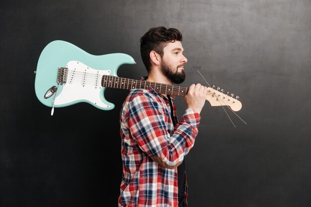 Porträt eines jungen Mannes, der in einem Hemd in einem Käfig auf einer Tafel steht, während er die Gitarre hält