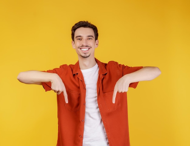 Porträt eines jungen Mannes, der mit dem Finger auf den Kopierraum zeigt, der auf gelbem Studiohintergrund isoliert ist