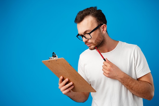 Porträt eines jungen Mannes, der Notizen in der Zwischenablage vor blauem Hintergrund macht