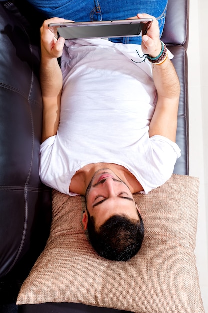 Porträt eines jungen Mannes, der sich auf einer Couch mit einer Tablette entspannt.