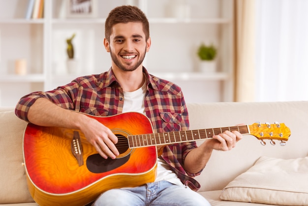 Porträt eines jungen Mannes, der zu Hause die Gitarre spielt.