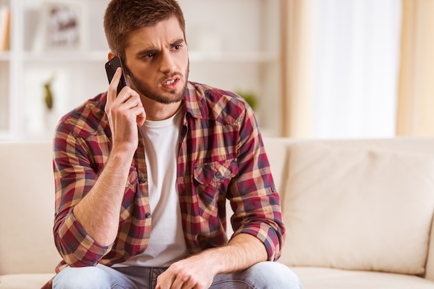 Porträt eines jungen Mannes, der zu Hause Telefon verwendet.