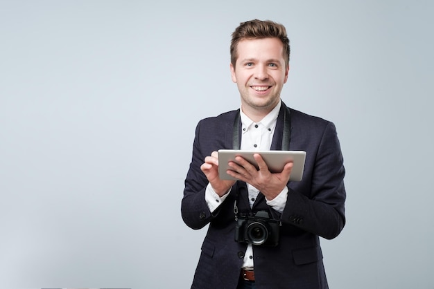 Porträt eines jungen Mannes im Anzug mit Tablet-Computer auf grauem Hintergrund und Blick in die Kamera