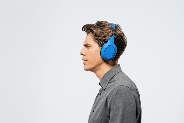 Porträt eines jungen Mannes im grauen Outfit, der seitlich steht und Musik mit blauen kabellosen Kopfhörern hört