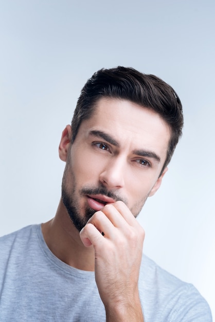 Porträt eines jungen Mannes im grauen T-Shirt, das gegen eine weiße Wand aufwirft