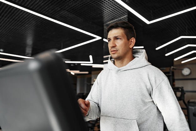 Porträt eines jungen Mannes in orangefarbenem Windbreaker-Training auf einem Fitnessgerät im Fitnessstudio