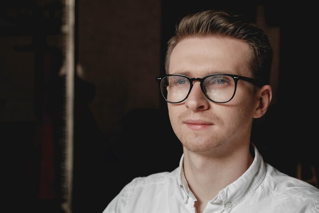 Porträt eines jungen Mannes mit Brille und weißem Hemd auf dunklem Hintergrund