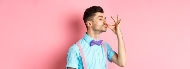 Porträt eines jungen Mannes mit gekreuzten Armen, der vor einem rosa Hintergrund steht