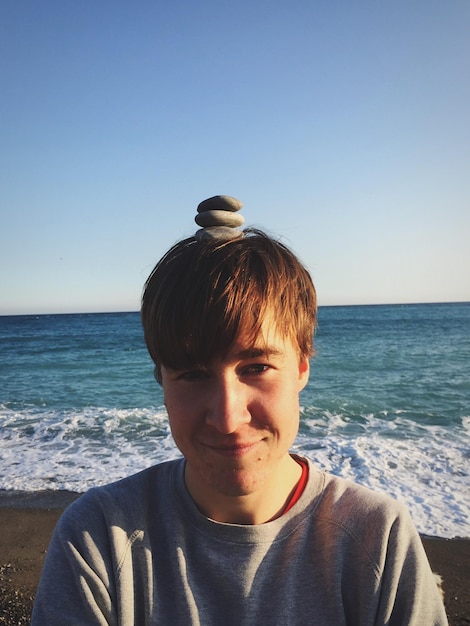 Foto porträt eines jungen mannes mit kieselsteinen auf dem kopf am strand vor klarem himmel