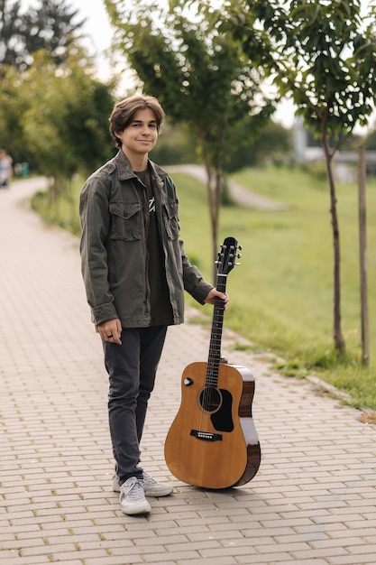 Porträt eines Jungen mit langen Haaren, der sich auf das Spielen von Gitarre im Freien vorbereitet