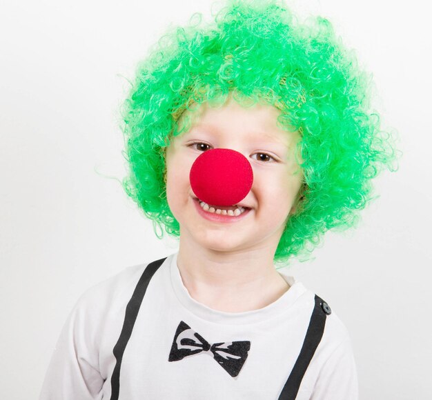 Porträt eines Jungen mit Perücke und Clowns-Nase auf weißem Hintergrund