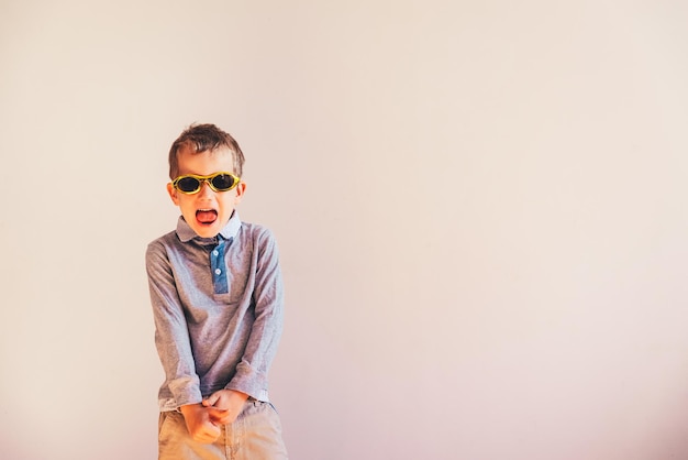 Porträt eines Jungen mit Sonnenbrille und offenem Mund, der an der Wand steht