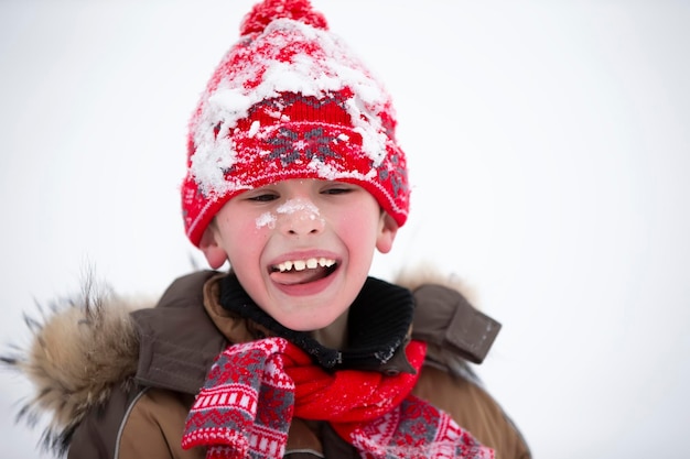 Porträt eines Jungen mit Wintermütze im Schnee. Fröhliches Kind spielt an einem Wintertag.