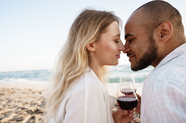 Porträt eines jungen Paares, das am Strand sitzt und Wein trinkt, Nahaufnahme