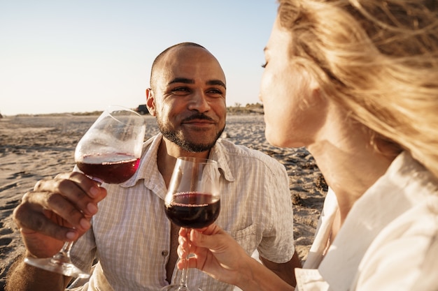 Porträt eines jungen Paares, das am Strand sitzt und Wein trinkt