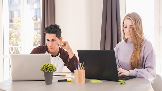 Porträt eines jungen Paares, das Laptops benutzt, während es fern von zu Hause arbeitet. Business- und Home-Office-Konzept.