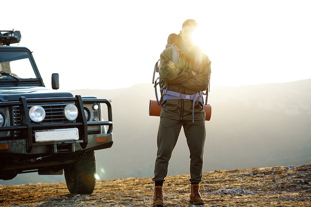 Porträt eines jungen Reisenden in Wanderausrüstung, der nahe seinem Geländewagen steht