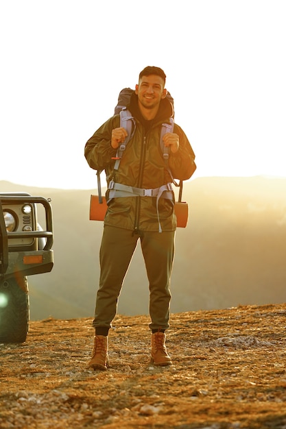 Porträt eines jungen Reisenden in Wanderausrüstung, der nahe seinem Geländewagen steht