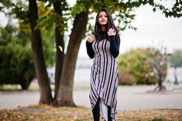 Porträt eines jungen schönen indischen oder südasiatischen Teenager-Mädchens im Kleid, das im Herbstpark posiert