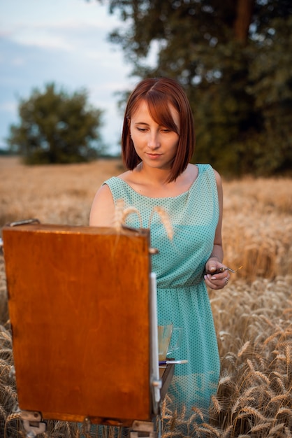 Porträt eines jungen schönen Mädchens, das Bild auf dem Gebiet des reifen Weizens malt