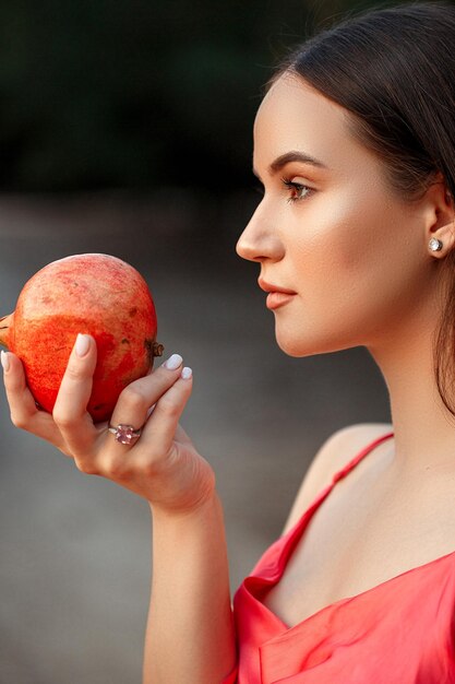 Porträt eines jungen schönen Mädchens mit einem Granatapfel in ihrem handsin einem roten Kleid flacher DOF-selektiver Fokus