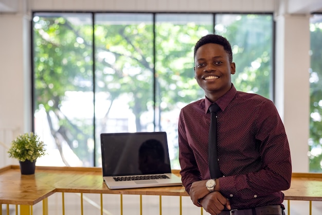 Porträt eines jungen schwarzen Mannes, der einen Laptop in einer Arbeitsumgebung verwendet, entweder ein afrikanischer Geschäftsmann oder ein Student.