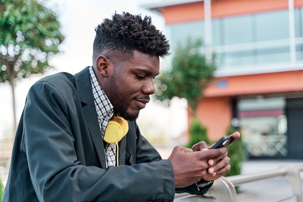 Porträt eines jungen schwarzen Mannes, der mit seinem Handy spricht und auf seinem Smartphone in der Stadt schreibt