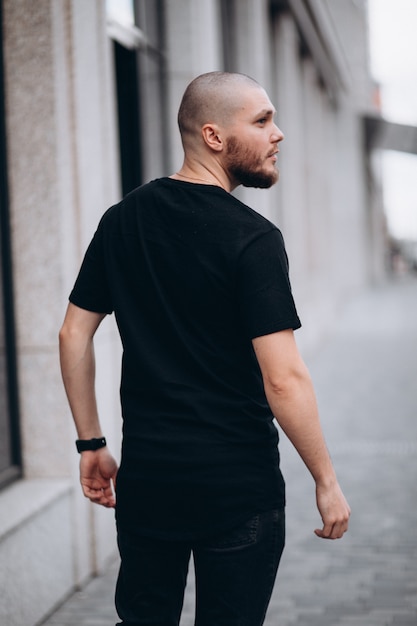 Porträt eines kahlen gutaussehenden bärtigen Mannes in einem schwarzen T-Shirt auf der Straße, der wegschaut