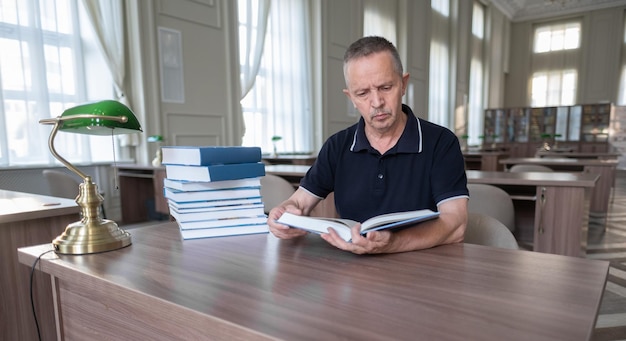 Porträt eines kaukasischen älteren Mannes, der mit einem Buch in einer öffentlichen Bibliothek arbeitet