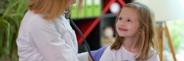 Foto porträt eines kinderarztes, der ein kleines lächelndes mädchen mit stethoskop untersucht. lächelndes kind an