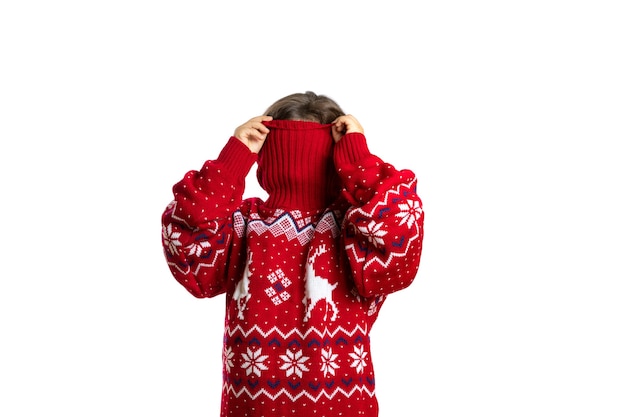Porträt eines Kindes im übergroßen roten Weihnachtsstrickpullover mit Rentierversteckgesicht im Krageniso...