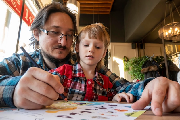 Porträt eines Kindes mit seinem Vater, der im Café mit Bleistiften zeichnet