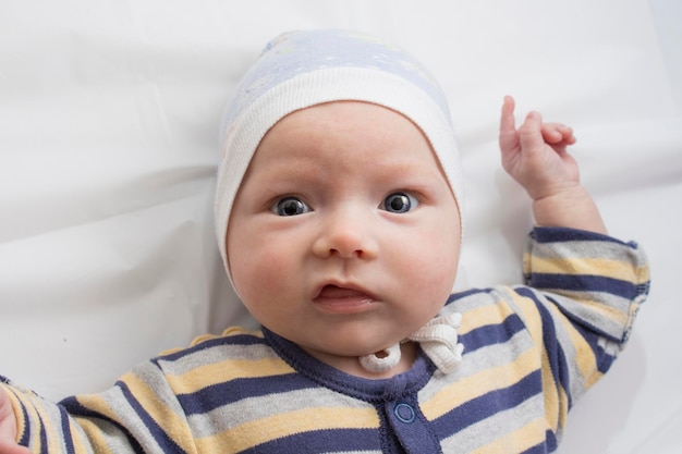Porträt eines kleinen Babys mit einem lustigen Gesichtsausdruck auf weißem Blatt. Flache Lage, Ansicht von oben.