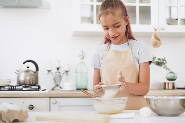 Porträt eines kleinen blonden jugendlich Mädchens mit Schürze in der Küche