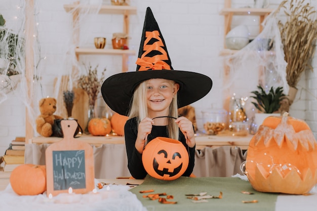 Porträt eines kleinen blonden Mädchens in einem Hexenkostüm mit riesigem Hexenhut-Halloween-Konzept