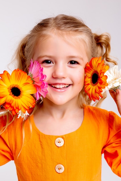 Porträt eines kleinen blonden Mädchens mit einem Blumenstrauß der Frühlingsblumen auf einer hellen Wand