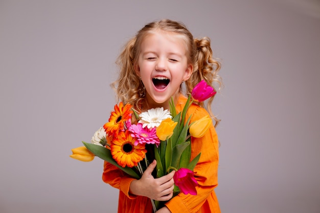 Porträt eines kleinen blonden Mädchens mit einem Blumenstrauß der Frühlingsblumen auf einer hellen Wand