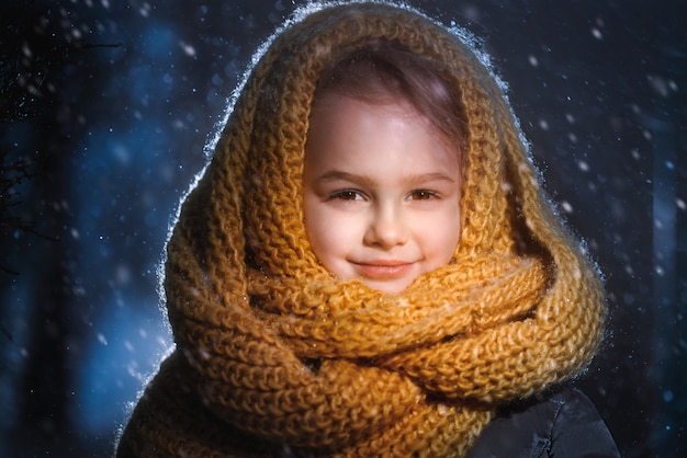 Porträt eines kleinen charmanten Mädchens in einem gelben Wollschal, das während eines Schneesturms draußen steht.