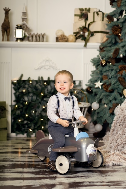 Porträt eines kleinen Jungen, der auf einem Weinlesespielzeugflugzeug nahe einem Weihnachtsbaum sitzt