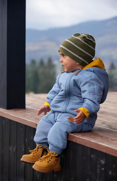 Foto porträt eines kleinen jungen, der auf einer holzterrasse sitzt und die aussicht genießt