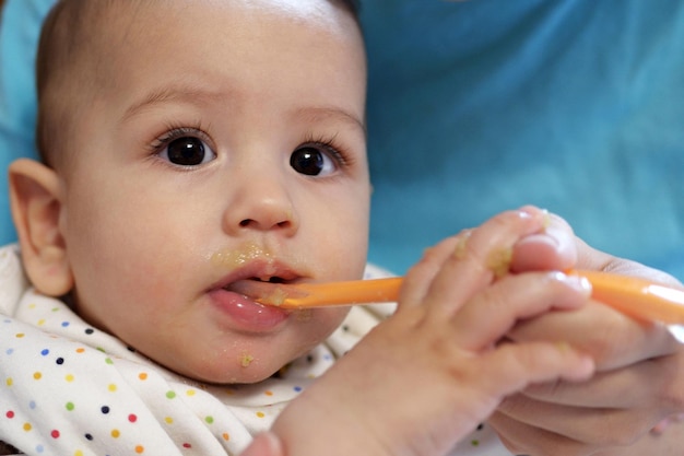 Porträt eines kleinen Jungen, der Nahrung isst. Baby mit einem Löffel im Fütterungsstuhl. Niedliches Baby, das seine erste Mahlzeit isst