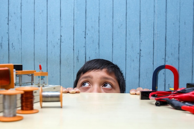 Porträt eines kleinen Jungen, der unter dem Tisch mit STEM-Projekt auf dem Tisch hervorschaut. Schüler, der ist