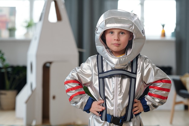 Porträt eines kleinen Jungen im Astronautenkostüm, der beim Spielen zu Hause in die Kamera schaut