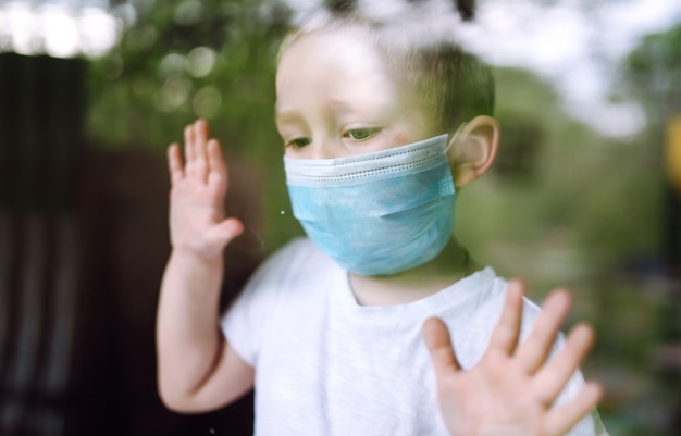 Porträt eines kleinen Jungen mit medizinischer Gesichtsmaske, der die Kamera in der Stadt betrachtet